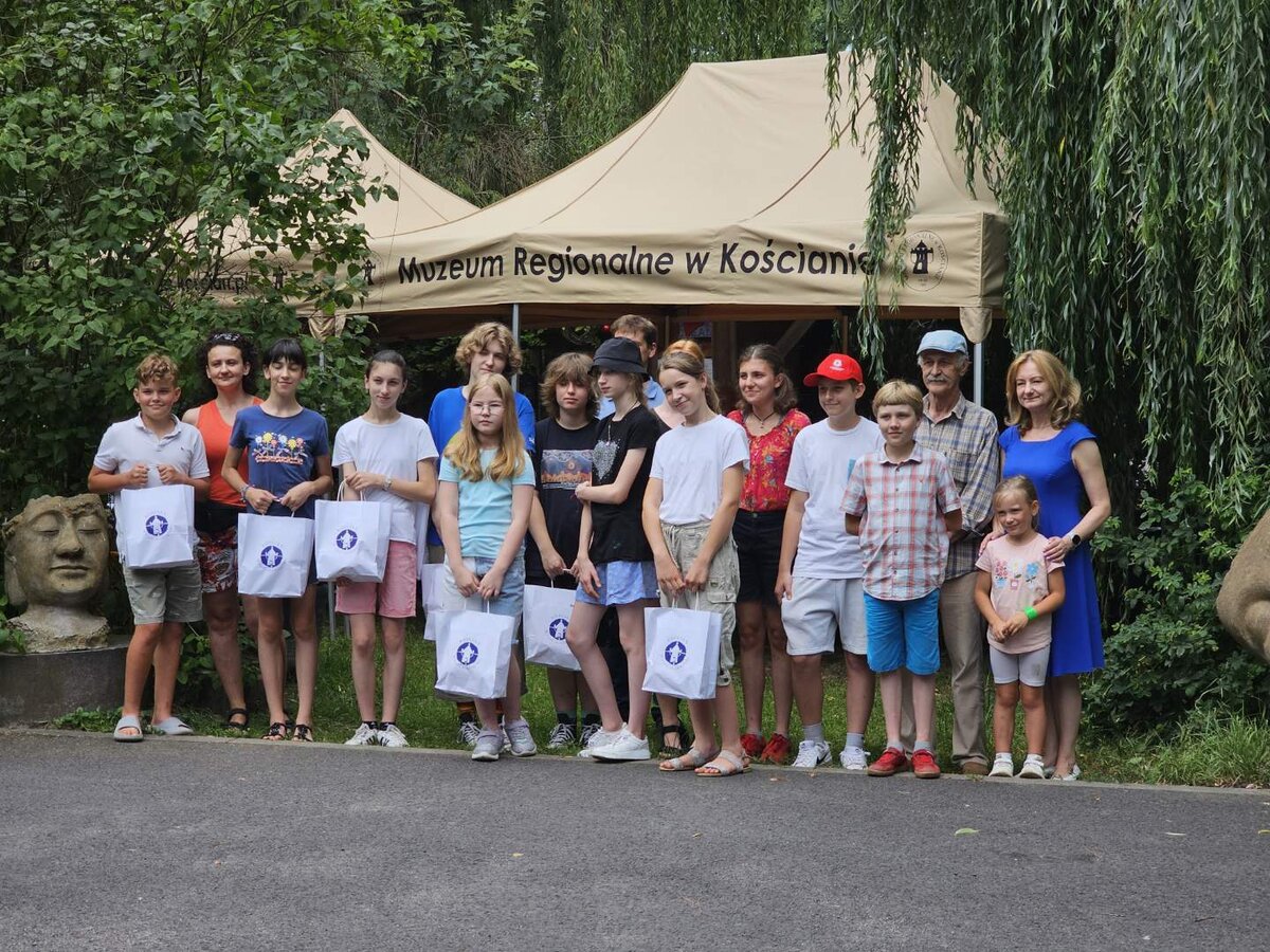 Zdjęcie grupowe młodych uczestników warsztatów rzeźbiarskich trzymających torby z upominkami na tle 